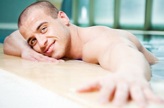 Young attractive male posing in a swimming pool, arm stretched