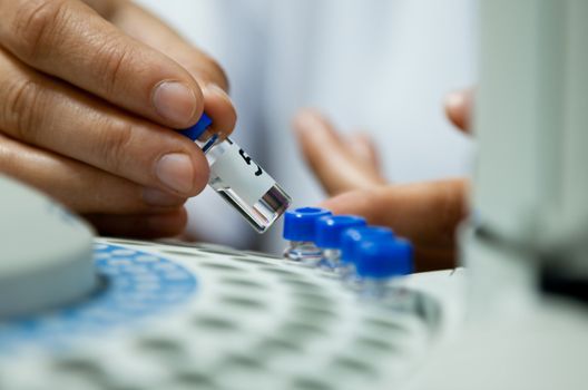 laborant inserting laboratory glass bottle in a chromatograph vial