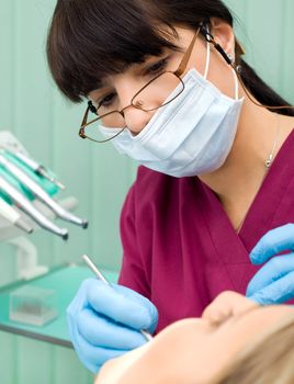Female dentist with protection mask and gloves examining patient