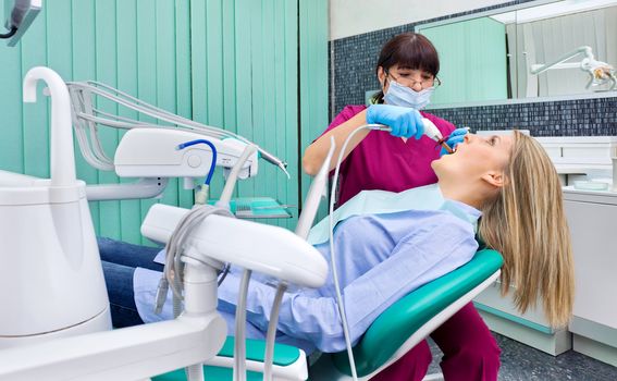Female dentist with protective mask and gloves working on patient in dental surgery