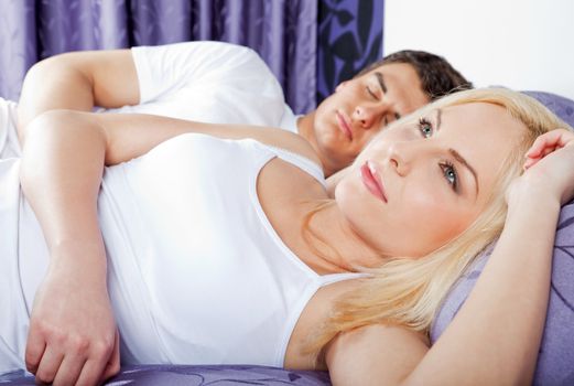 Young couple lying in bed, focus on female awake thinking