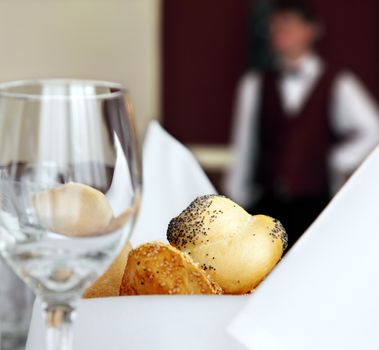 table setting in restaurant with bread empty glass and waiter off focus