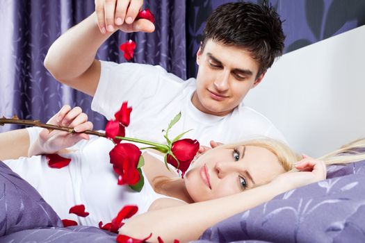 romantic couple in bed, female holding red rose, male releases petals