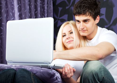 Attractive young couple using white laptop in bed togather