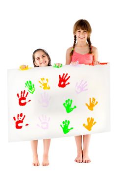 Two smiling barefoot little girls holding white sheet with colourful hand prints