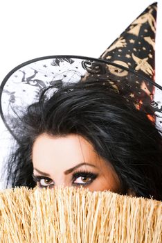 Young female as a witch hiding behind broom, looking at camera