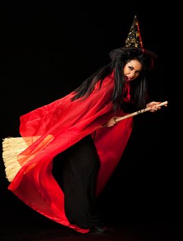 witch with a red cloak, hat and a broom between her legs