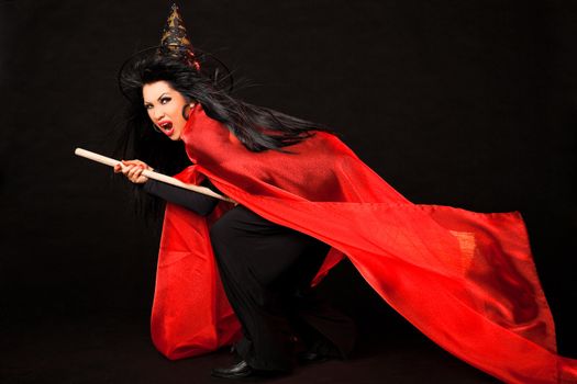 Female in witch costume with red cloak and broom between her legs screaming