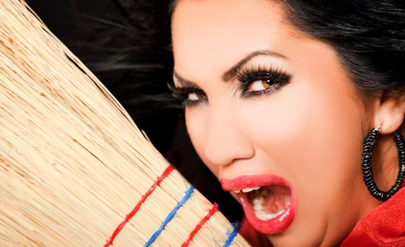 Close-up of female face looking evul at camera, holding a broom screaming