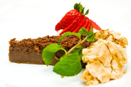 Close-up of slice of chocolate cake decorated with mint and strawberry on white background