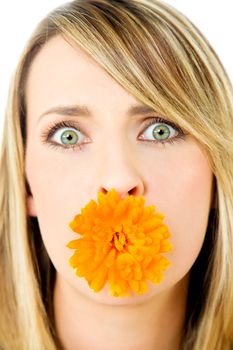 Close-up of beautiful blond female with marigold flower in mouth, staring at camera