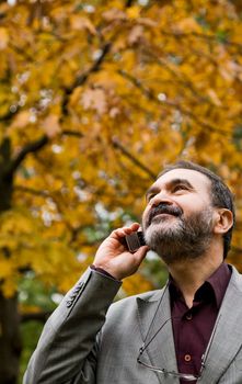 Portrait of positive adult man talking on mobile phone, autumn day, looking up