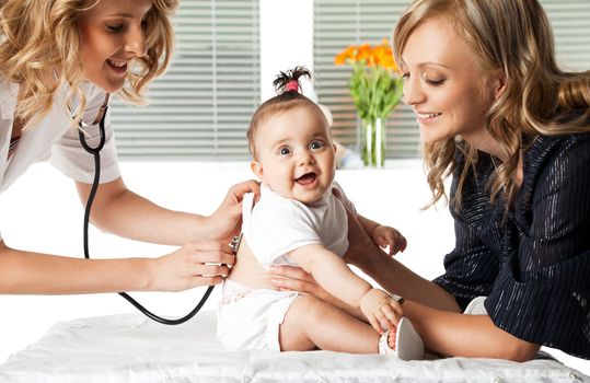 Female doctor examining little smiling baby girl held by her mother