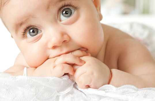 Close-up of adorable little baby face lying with hand in mouth, looking up