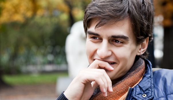 Close-up of happy male sitting in park and smiling, hand under chin