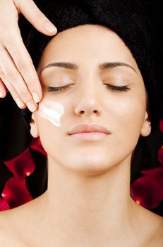 A young beautiful woman receiving moisturizing cream on cheek