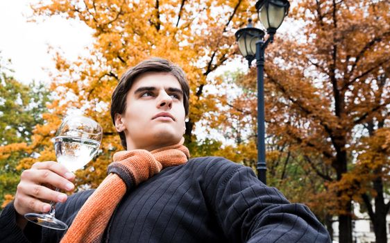 Portrait of young male holding glass of water in park on autumn day looking serious