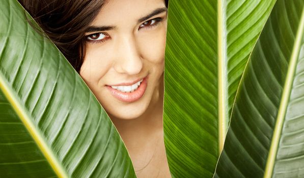 Beautiful young female posing with face between exotic flower leaves