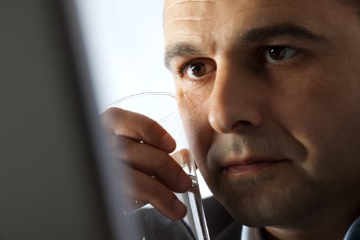 Close-up of a man holding a glass of water next to his face, looking at monitor