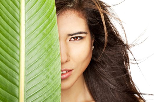 Beautiful young female face half hidden behind big leaf