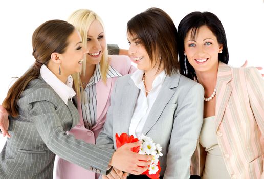 Team of four happy businesswomen hugging and smiling, one holding flowers