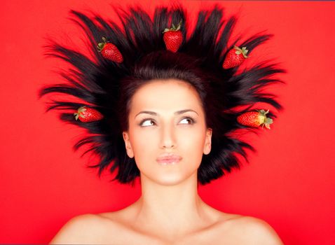 Portrait of young female with strawberries in her hair, on red background