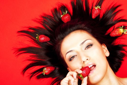 Portrait of woman lying, biting strawberry on red background