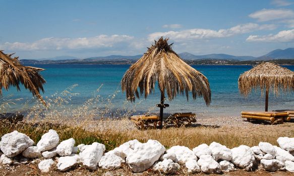 View of scenic beach with straw umbrellas and lounge chairs in Greece