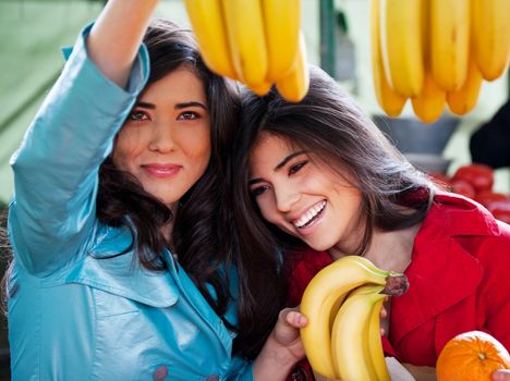 Two beautiful girls sister twins choosing bananas at farmers market