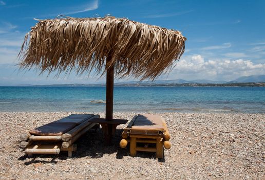 Two wooden lounge chairs under straw umbrella on beach, Greece
