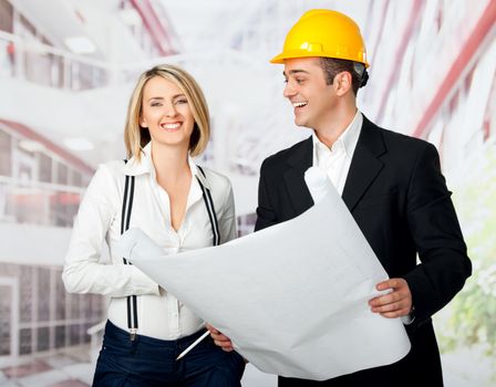 Male and female architects holding blueprint and smiling, man wearing yellow hardhat