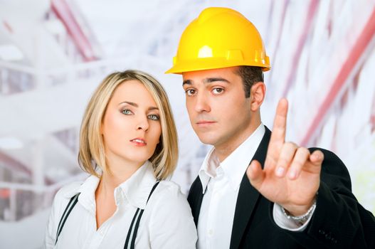 Male and female architects looking at camera, man wearing hardhat and pointing with finger