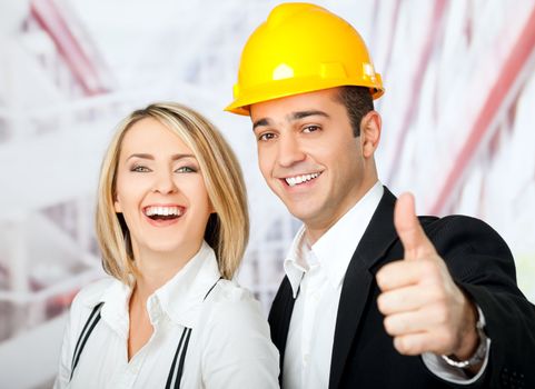 Male and female architects smiling at camera, man wearing hardhat and showing thumbs up