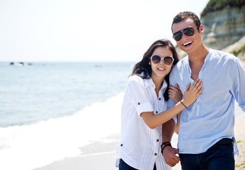 Young couple with sunglasses hugging and walking along beach