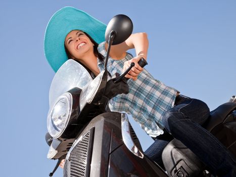 Beautiful smiling woman with blue hat riding moped