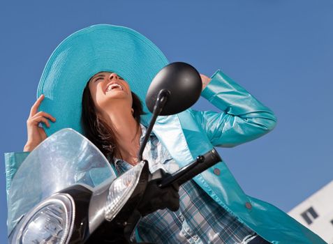 Happy woman with blue raincoat and hat sitting on moped loughing