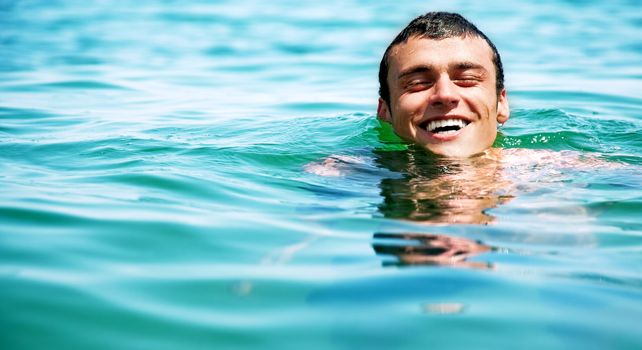 Handsome happy male swimming in sea and smiling