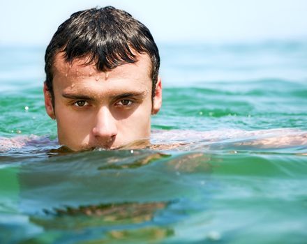 Close-up of young handsome male face in water, looking at camera