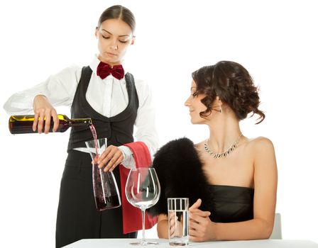 Beautiful elegant female sitting in restaurant while young waitress decanting wine