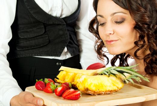 female looking at fresh sliced strawberries and pineapple on cutting board held by waitress