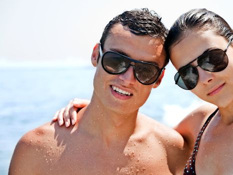 young couple with sunglasses hugging and posing on beach