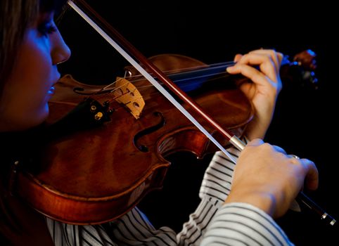 Young female violinist playing violin on black background