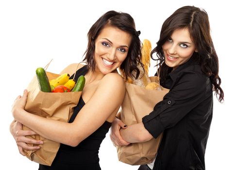 Two young smiling girlfriends holding grocery bags isolated