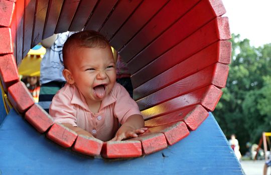 A joyful kid is sticking his tongue out while crawling in a playground tunnel