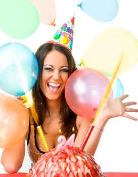 Happy female with party hat smiling over birthday cake and balloons