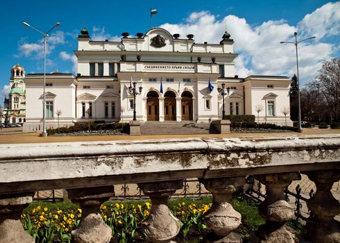 Front view of the Bulgarian National Assembly building through an old stone fence