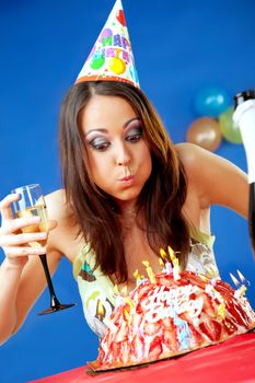 female with party hat blowing birthday cake candles, glass of wine in hand