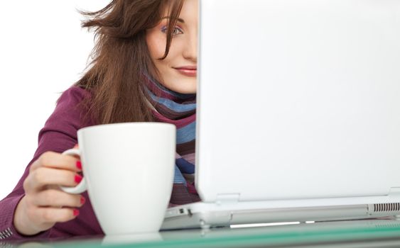 Young beautiful female sitting behind a laptop, holding a white cup