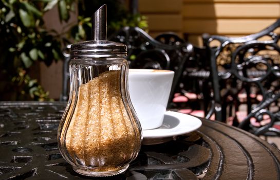 sugar-bowl on a cafe table, full of brown sugar with a cup of coffee behind