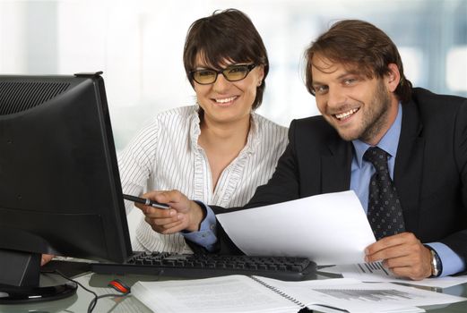 Two business people behind a monitor smiling at camera